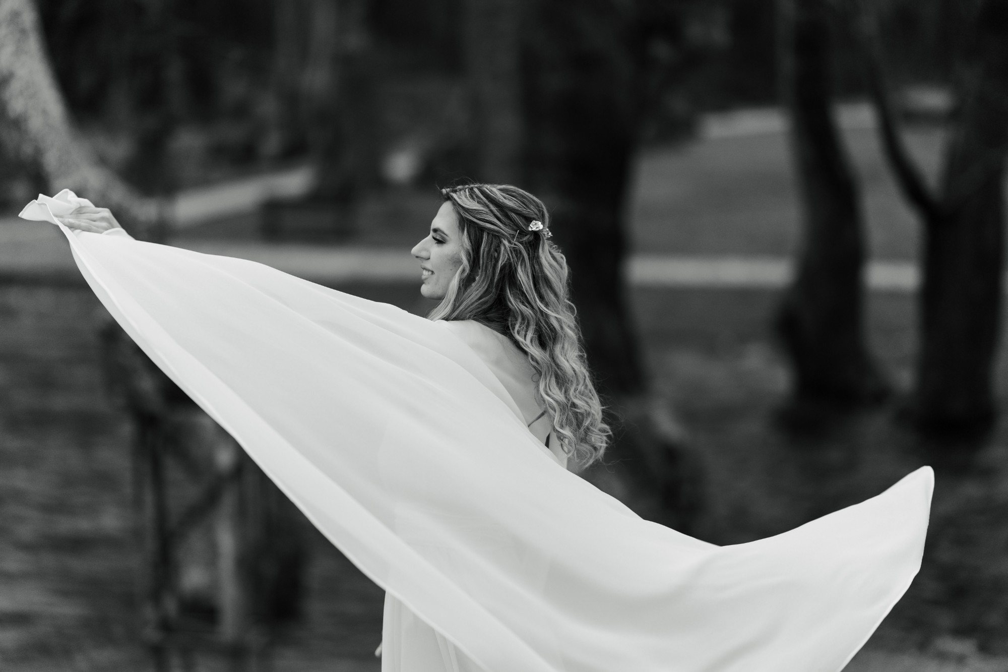 The bride twirls her long cape among the trees