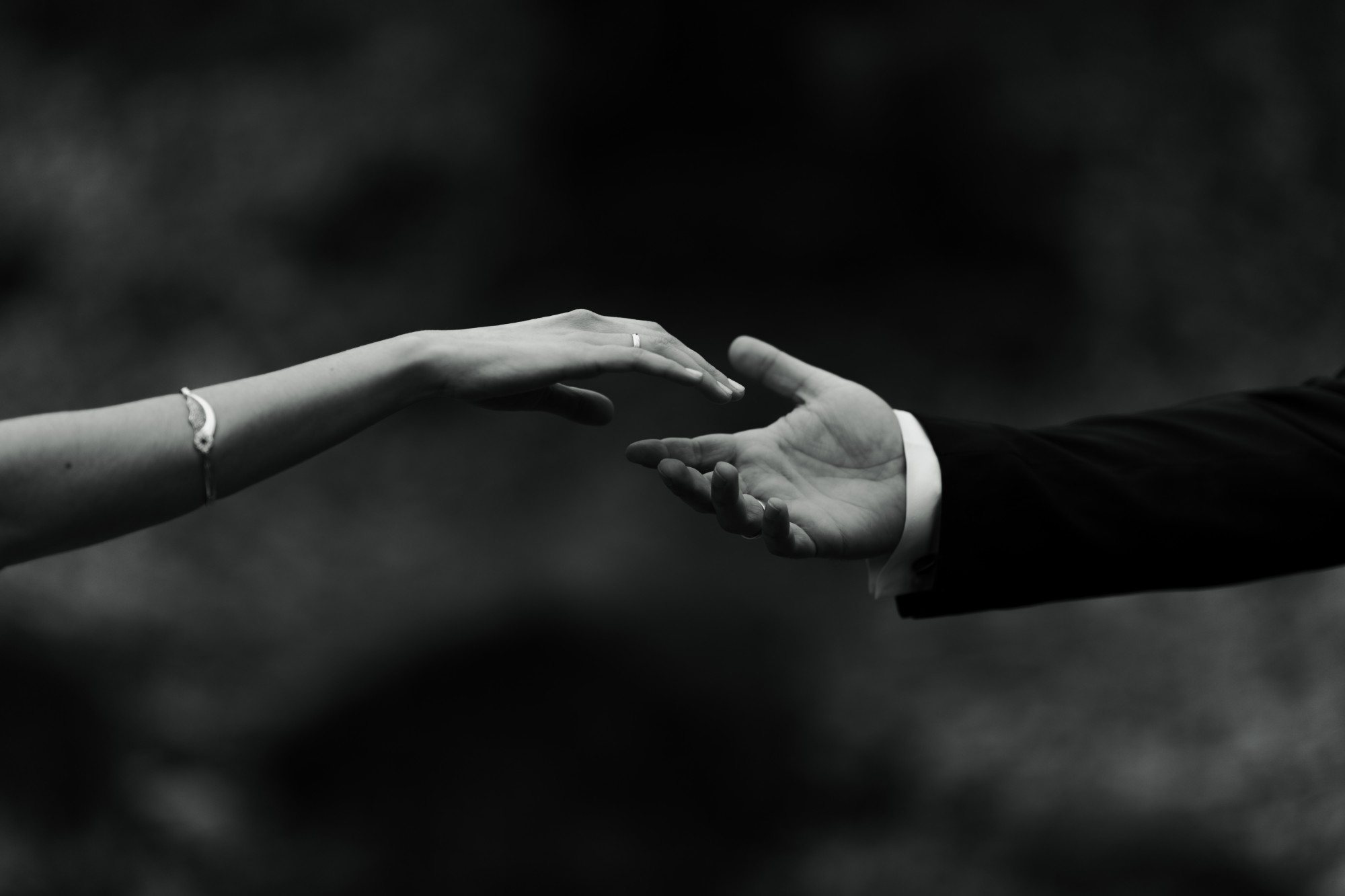 Bride and groom reach for each other’s hands, wedding rings on